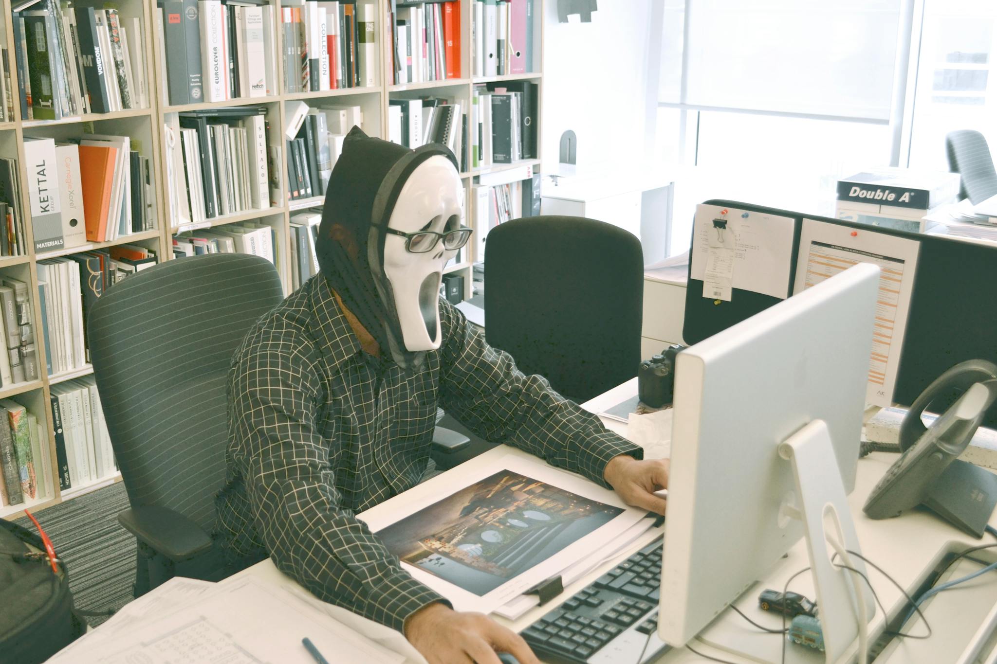 Person wearing a ghost mask working in an office environment filled with books.